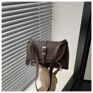 Détail du sac bandoulière en cuir marron foncé avec fermetures éclair et boucle magnétique