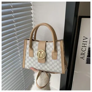 Detail of the elegant M-letter monogram pattern and golden circular metal clasp on tote bag