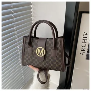 Detailed view of dark brown tote bag with M-pattern and gold circular metal hardware