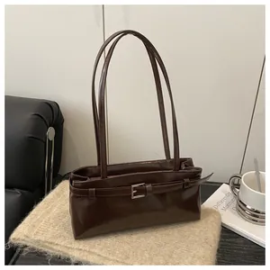 Détail d'un sac sous le bras en cuir marron foncé avec boucle décorative et anses longues