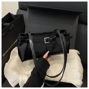 Détail du sac sous le bras noir brillant avec boucle argentée et texture de cuir lisse