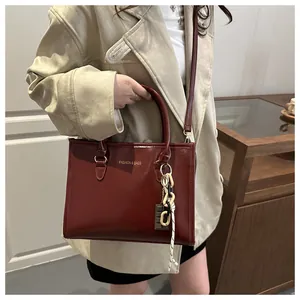 Détail d'un sac à main bordeaux avec logo doré et pendentif chaîne sur mannequin