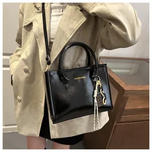 Détail du sac bandoulière en cuir verni noir avec chaîne porté sur un manteau beige