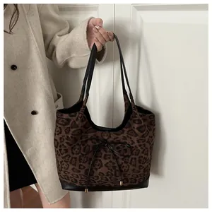Detailed view of leopard print tote bag with black leather straps on beige coat