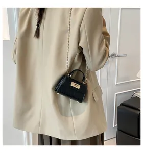 Detail of black faux crocodile leather mini bag with gold chain strap on casual model