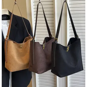 Three minimalist suede tote bags in camel, brown, and black with vintage gold buckles