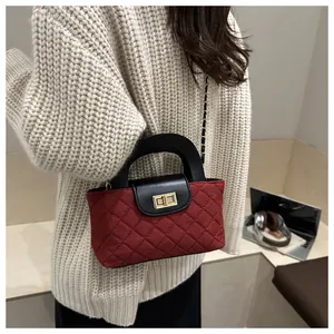 Detail of red quilted small square bag with golden twist lock and chain strap on model