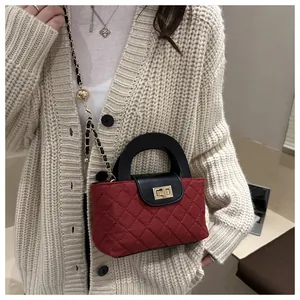 Close-up of quilted burgundy fabric texture and golden metal twist lock on a small square bag