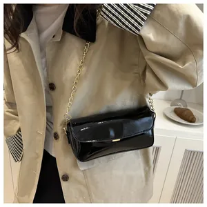 Close-up of black glossy oil wax leather shoulder bag with golden chain and metal detail