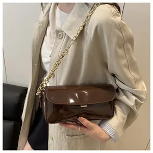 Detail of dark brown oil wax leather baguette bag with gold chain strap on model