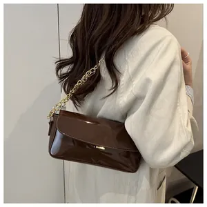 Detail of dark brown patent leather baguette bag with a chunky gold chain strap