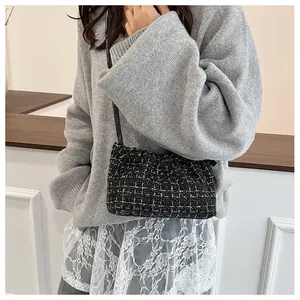 Detail of elegant black and gold tweed shoulder bag worn with a stylish knit sweater