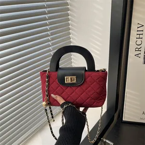 Burgundy quilted crossbody bag with gold chain strap and black handle in a stylish setting