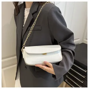 White glossy shoulder bag with gold chain strap and metallic buckle on suit