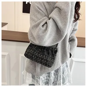 Detail of tweed underarm bag featuring elegant black and gold plaid pleats on a model