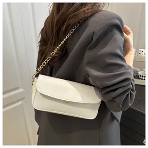 Chic white patent leather underarm bag with gold chain strap worn on a gray suit