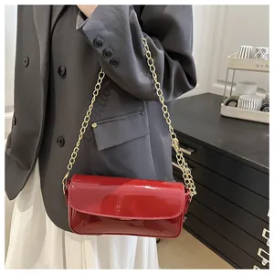 Fashionable red patent leather shoulder bag with gold chain strap on model's shoulder