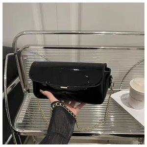 Macro view of black patent leather shoulder bag with gold metal trim and chain strap