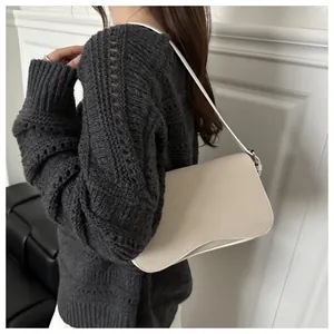 Close-up of minimalist off-white matte underarm bag worn with a grey knit sweater