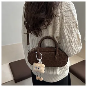Detail of leopard print suede baguette bag with a plush doll charm on a beige sweater background
