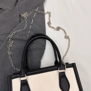 Detail of cream tote with grid texture, black leather handle and silver chain strap