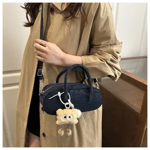 Detail of dark blue cylinder bag with leopard embossing and a yellow plush monster charm