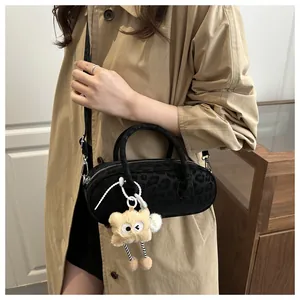 Detail of black leopard print barrel bag with a plush monster charm on a beige coat