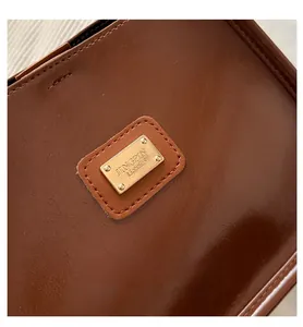 Close-up of brown leather texture and golden metal logo plaque on a shoulder bag