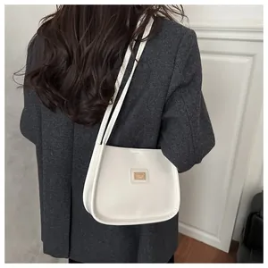 Detail view of the elegant white underarm bag with a gold rectangular logo plate