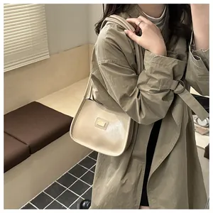 Detail of a cream leather hobo bag with a rectangular metal logo on a wooden background
