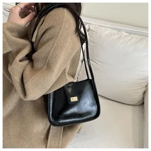 Detail of glossy black leather shoulder bag with gold logo on a camel wool coat