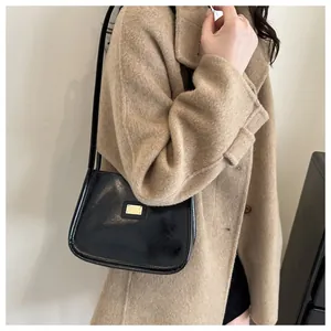 Detail view of a black glossy underarm bag with an elegant golden rectangular metal plate