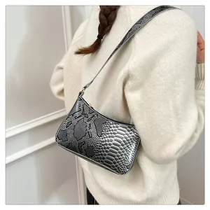 Détail du sac bandoulière argenté à motif serpent porté avec un pull en maille blanc