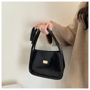 Close-up of black glossy leather underarm bag featuring a gold rectangular logo plate