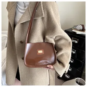 Detail of a brown leather underarm bag with gold metal plaque and sleek shoulder strap
