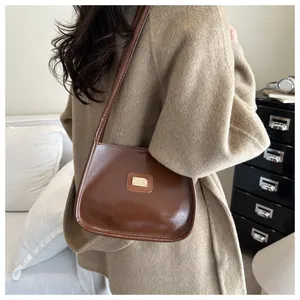 Detail of a brown glossy leather underarm bag with a golden metal plaque and sleek design