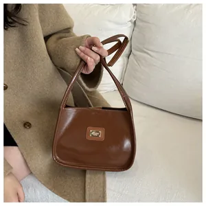 Close-up of caramel brown leather underarm bag with gold logo plaque and sleek texture