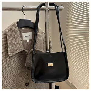 Detail view of black glossy leather underarm bag with gold metal logo on tweed coat