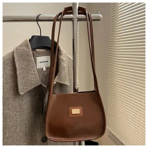 Close-up of a deep brown leather underarm bag with a gold metal plate and slim straps