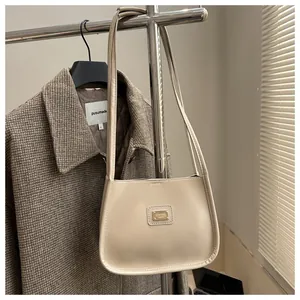 Detail of cream minimalist underarm bag with metal logo hanging on a rack