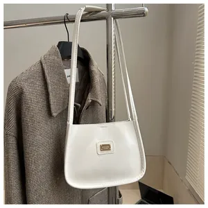 Detail of cream white underarm bag with gold metal plaque against a plaid coat background