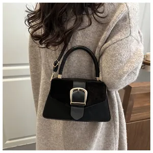 Detail of a black leather handbag featuring suede patchwork and a large gold metal buckle