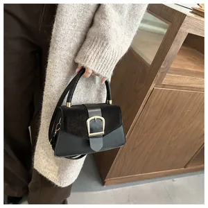 Detail of minimalist black crossbody bag with gold buckle and textured patchwork design