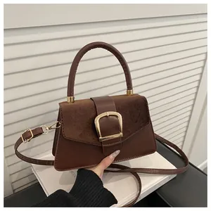 Detail of dark brown paneled crossbody bag with golden U-shaped buckle and top handle