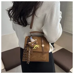 Close-up of brown suede bag featuring cartoon bear motifs and 3D plush bear charm