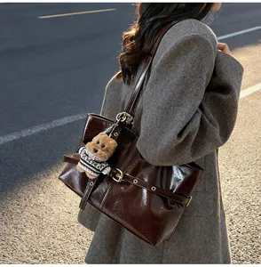 Détail du cabas en cuir ciré marron foncé avec charm d'ours porté à l'épaule du modèle