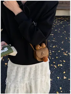 Dettaglio borsa a tracolla marrone con grande fiocco e accessorio con pompon morbido