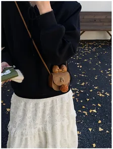 Bambina con borsa a tracolla a forma di orso marrone con fiocco e pompon all'aperto