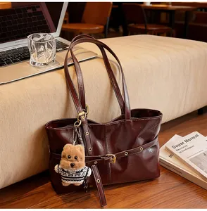 Détail d'un sac cabas en cuir marron foncé avec un pendentif ours et des boucles dorées