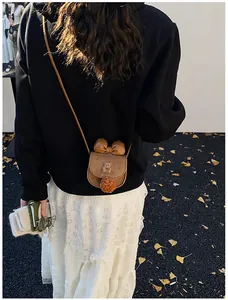 Graziosa borsa a tracolla marrone da ragazza con fiocco e pompon in scena all'aperto